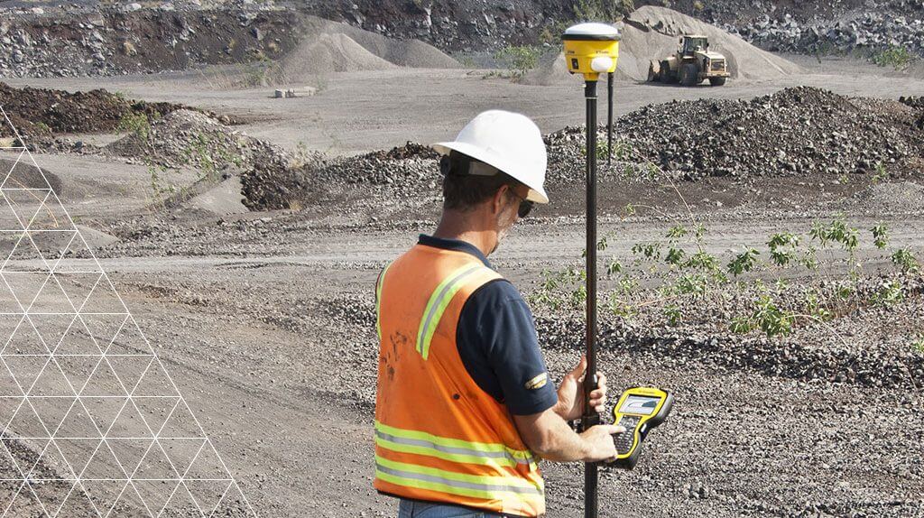 Person in high-visibility clothing using surveying equipment in an open-pit mine.